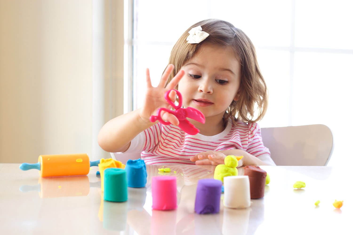 Play-Doh scissors held up by girl surrounded by Play-Doh.
