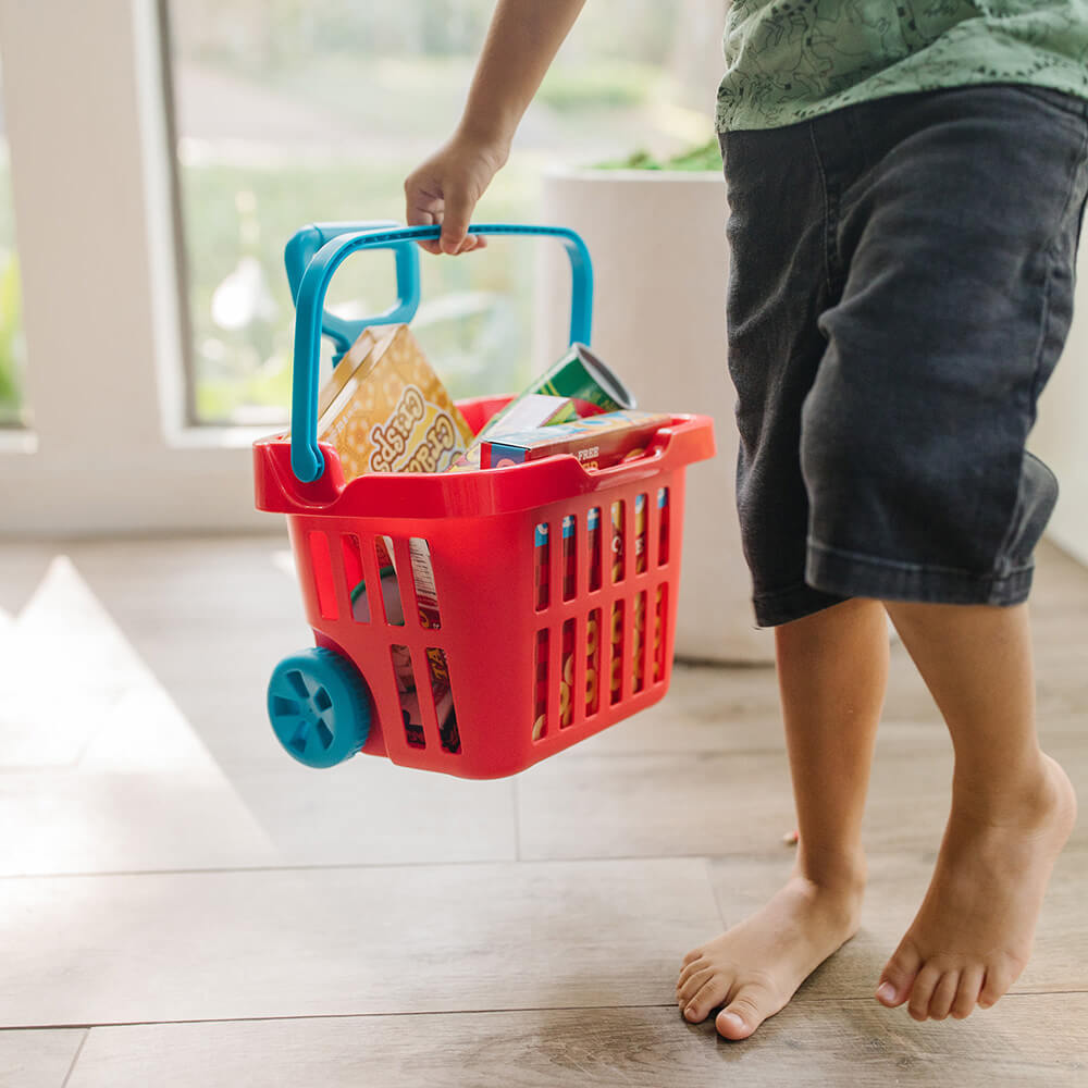 Boy is playing with and holding the Melissa and Doug Fill & Roll Grocery Basket Play Set, which can be carried by its blue handle