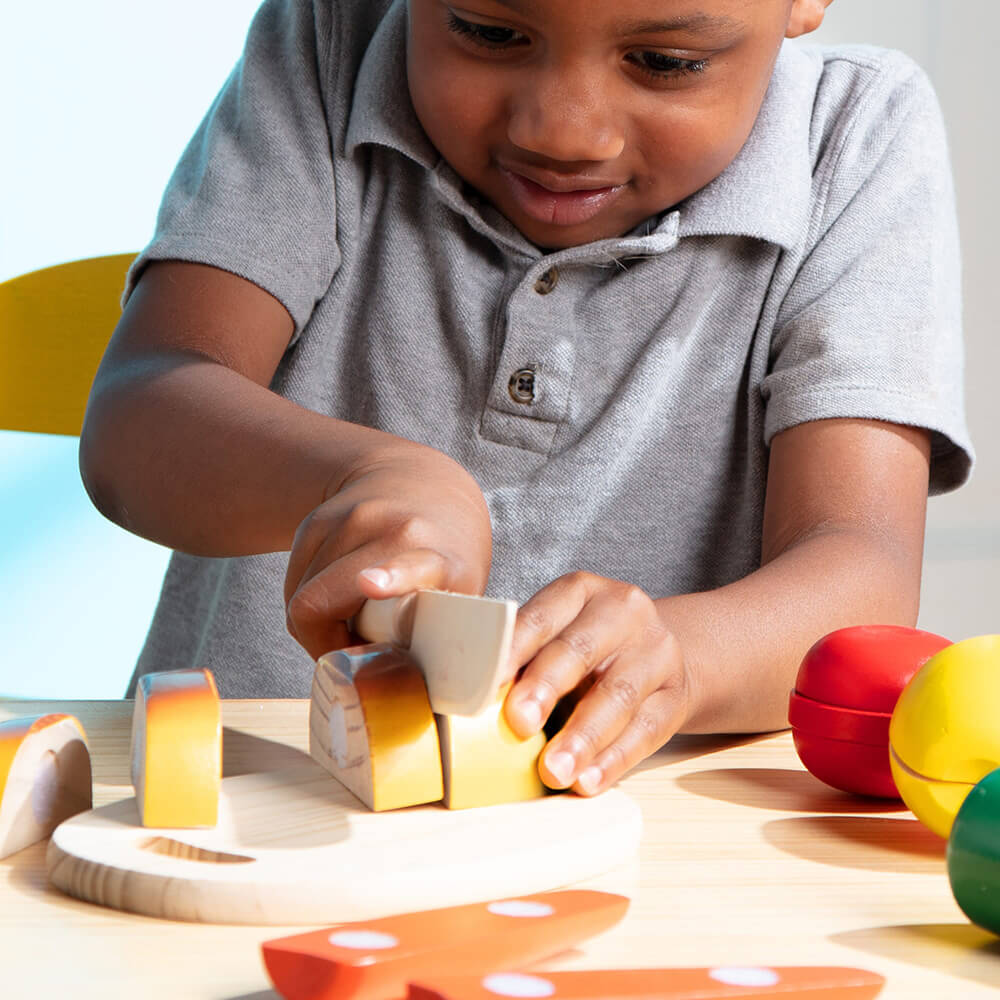 Little boy playing with the Melissa and Doug Cutting Food Wooden Food Play Set cutting the bread with the knife on the cutting board