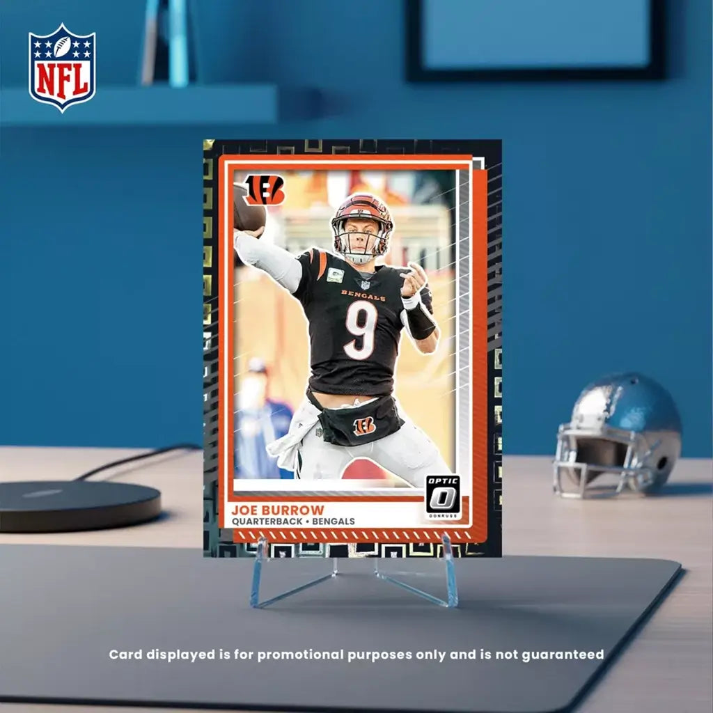 Panini Donruss Optic NFL football card display in black, orange, and white printed cardstock with rectangular shape, featuring quarterback image on stand, collector showcase on desk setting background