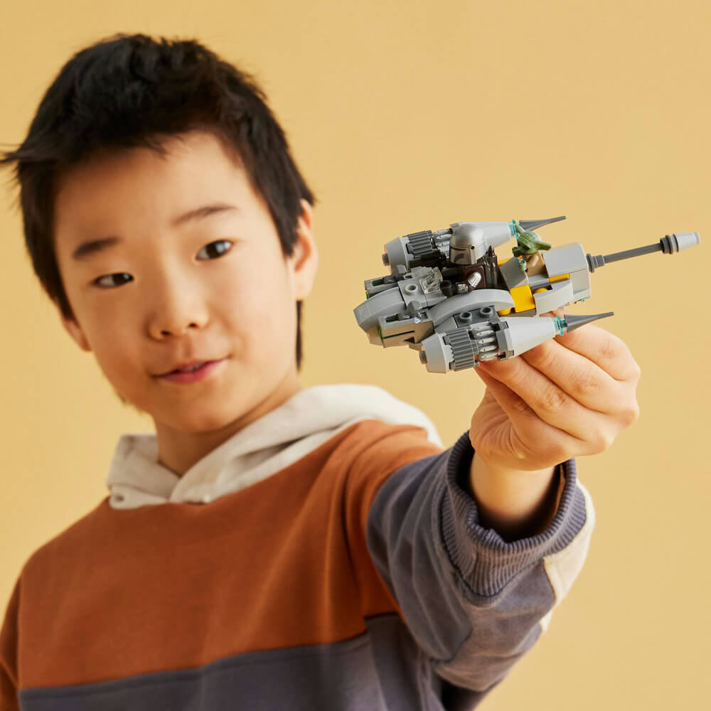 Boy shown flying the LEGO® Star Wars™ The Mandalorian’s N-1 Starfighter™ Microfighter 75363 (88 Pieces) with his hand