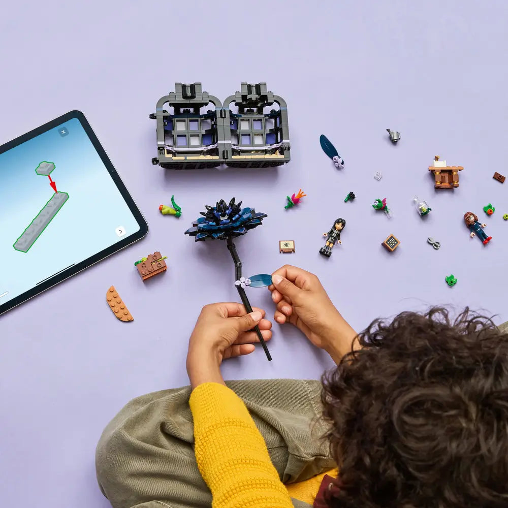 Overhead view of child assembling the LEGO Black Dahlia Flower set from Wednesday, surrounded by colorful bricks, mini-dolls, accessories, and a tablet displaying digital building instructions.