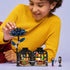 Smiling child in yellow sweater plays with the LEGO Black Dahlia Flower set from Wednesday, showing the tall dark flower connected to an open buildable greenhouse with vibrant plant details and mini-dolls.