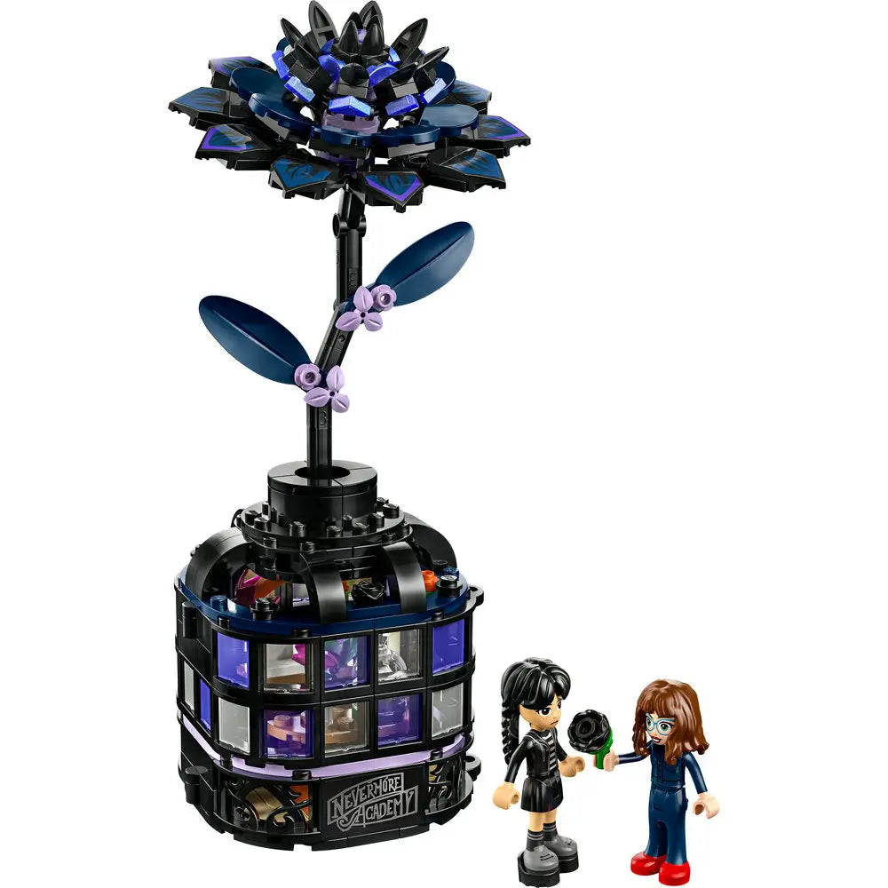 Fully assembled LEGO Wednesday Addams Black Dahlia Flower set displayed on white background, featuring two mini-doll figures, a tall stylized dark flower, and a gothic glass dome base marked "Nevermore Academy.