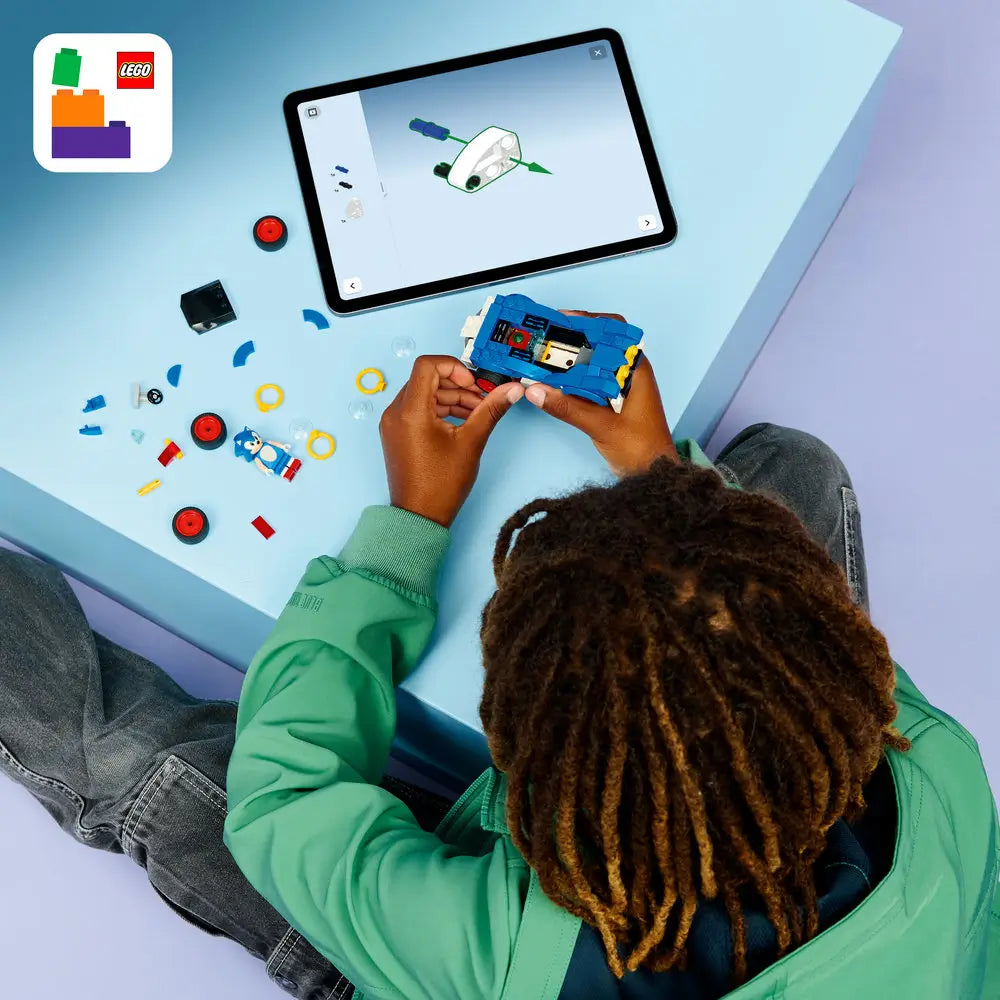 LEGO Sonic the Hedgehog building pieces in blue, white, red, and yellow plastic with wheels, Sonic character figure, and ring accessories, scattered flat for assembly to clearly display all components on a light tabletop surface.