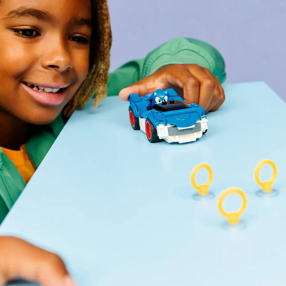 Child assembling LEGO Sonic the Hedgehog Speedster Lightning car made of blue plastic with red wheels, holding the model at hand scale to demonstrate interactive building and imaginative play in a bright indoor setting.