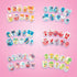 Close-up of Aquabeads Nail Studio decorated nail sets featuring pastel designs with bows, hearts, rainbows, and fruit patterns arranged on a pink background.