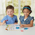 Two children at a white table smiling as they create Disney Aquabeads Stitch designs, surrounded by colorful bead pieces and a crafting guide in a bright indoor playroom.