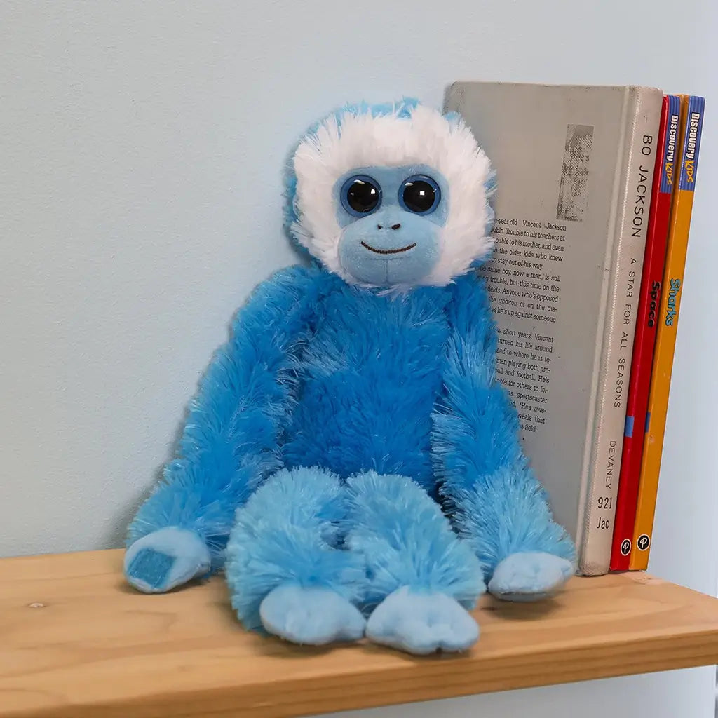 Aurora hanging monkey plush featuring vibrant blue fluffy polyester texture, elongated limbs with hook style hands, relaxed seated form, and friendly expression, displayed on a shelf in a child bedroom setting.