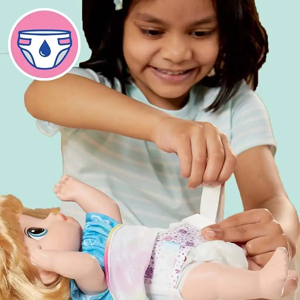 Child fastening a printed white diaper onto Baby Alive doll, showing nurturing pretend play while the doll lies on its back against a soft pastel backdrop.