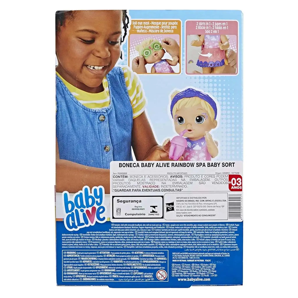 Baby Alive Rainbow Spa Baby package back shows a smiling child placing a cucumber-print mask on the blonde doll, with accessory callouts, illustrated instructions, and multilingual safety and brand text filling the blue lower panel.