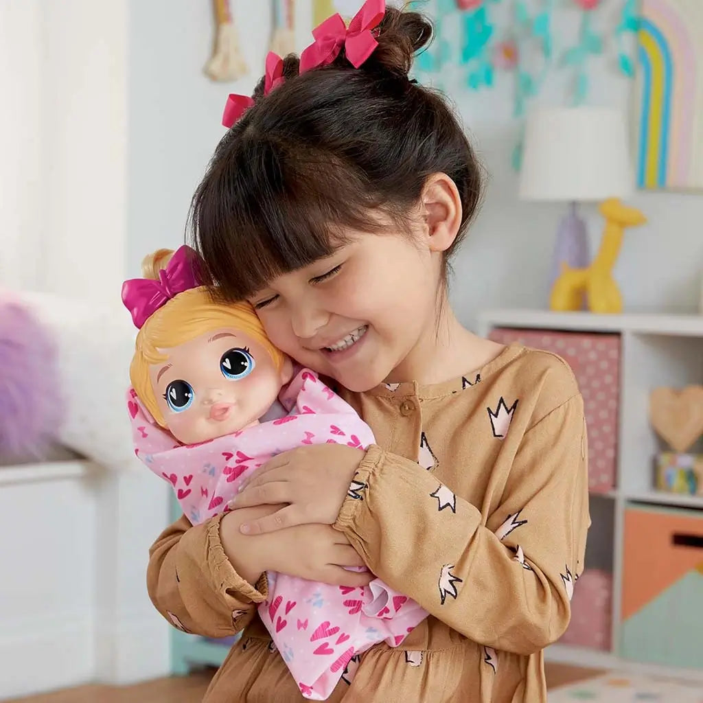 Child hugging Baby Alive Harper Hugs doll wrapped warmly in pink heart-print blanket inside a cozy bedroom setting, highlighting comforting nurturing play moments.