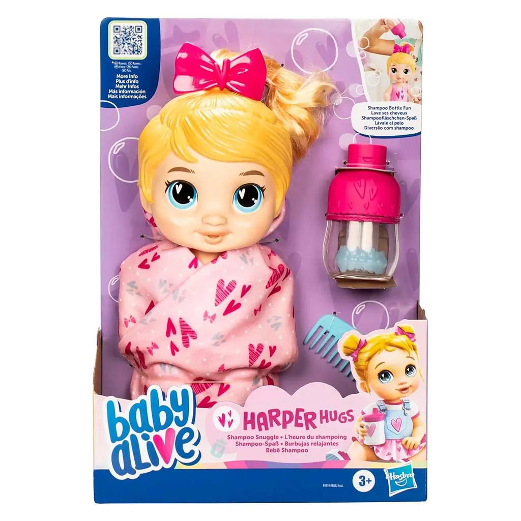 Baby Alive Harper Hugs packaged doll wrapped in pink heart-print blanket with included bottle and comb visible through display window, set on purple bubbly branding background.