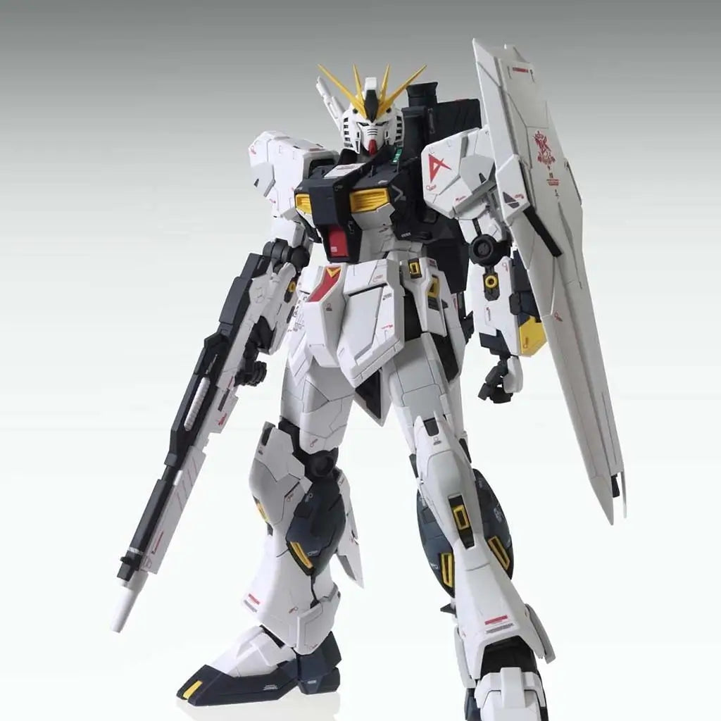 Gundam plastic model Bandai RX-93 Nu Gundam shows white and dark panels with crisp mechanical detailing, sharp armor edges, and an elevated shield stance in a softly lit gradient studio environment.