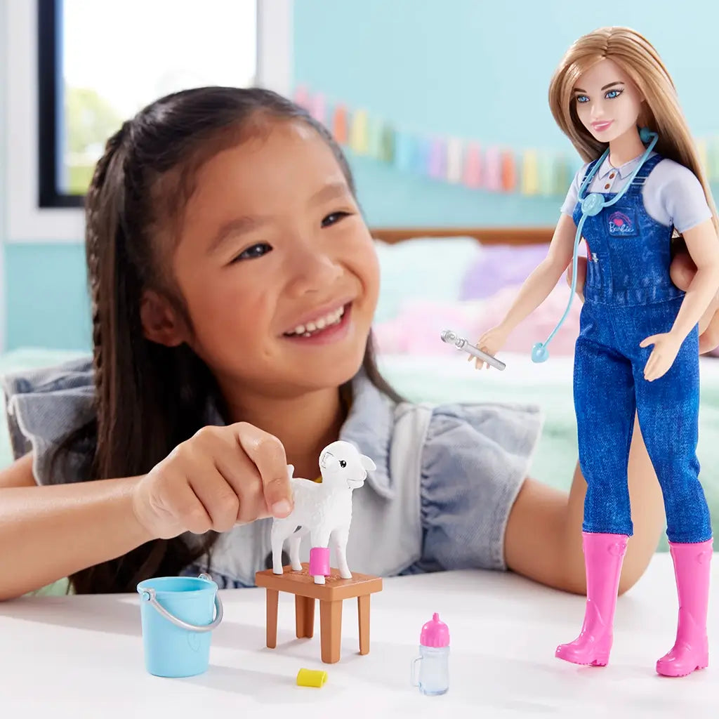 Smiling child playing with Barbie farm vet doll, placing a cast on a white lamb toy while Barbie holds medical tools, encouraging imaginative animal care play.