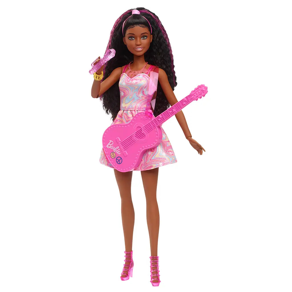 Barbie 65th Anniversary Pop Star Doll posed holding a pink guitar and microphone, wearing a pastel swirl dress with matching pink heels and headband, styled for musical play.