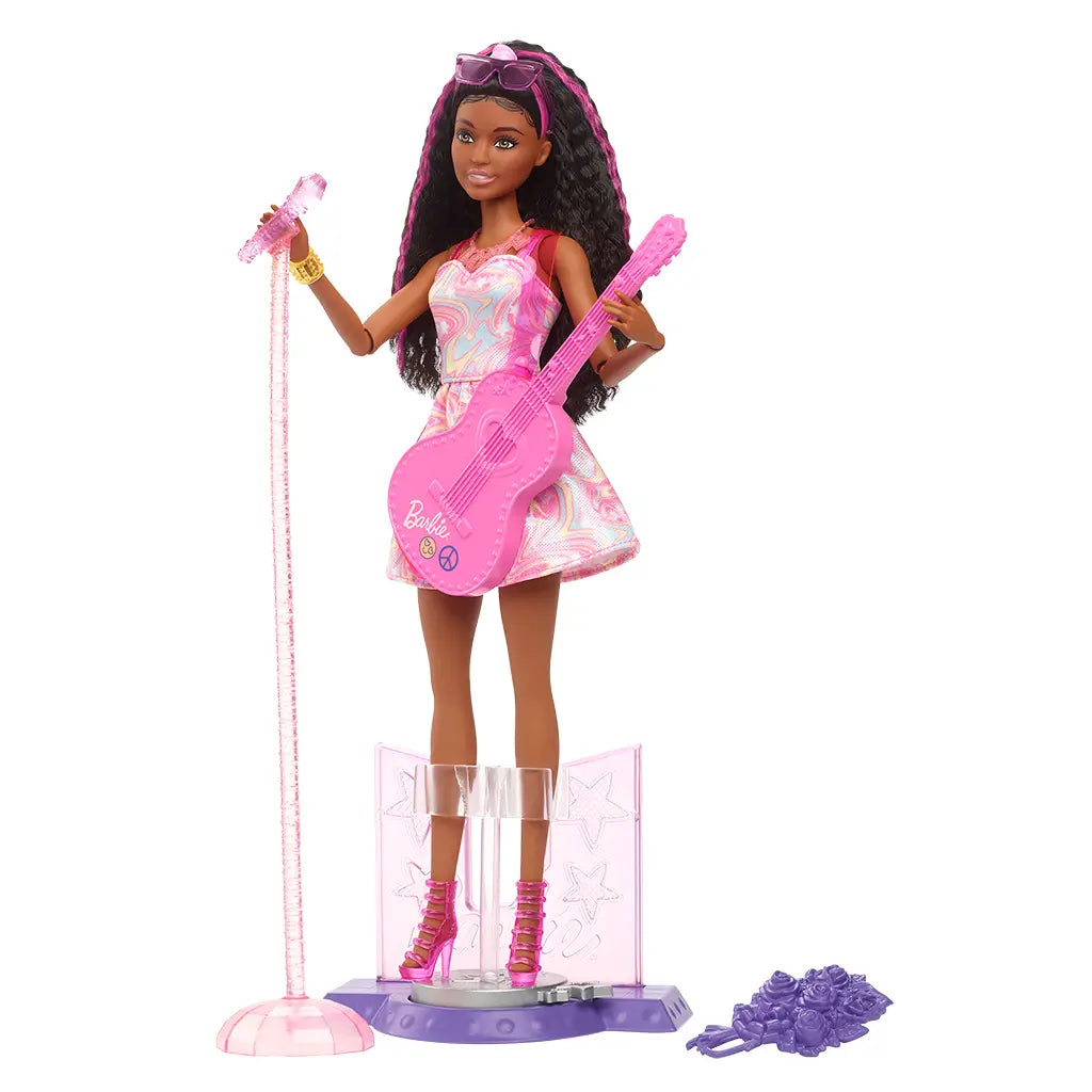 Barbie 65th Anniversary Pop Star Doll displayed on stage stand with microphone, pink guitar, pastel swirl dress, and accessories including bouquet, sunglasses, and jewelry.
