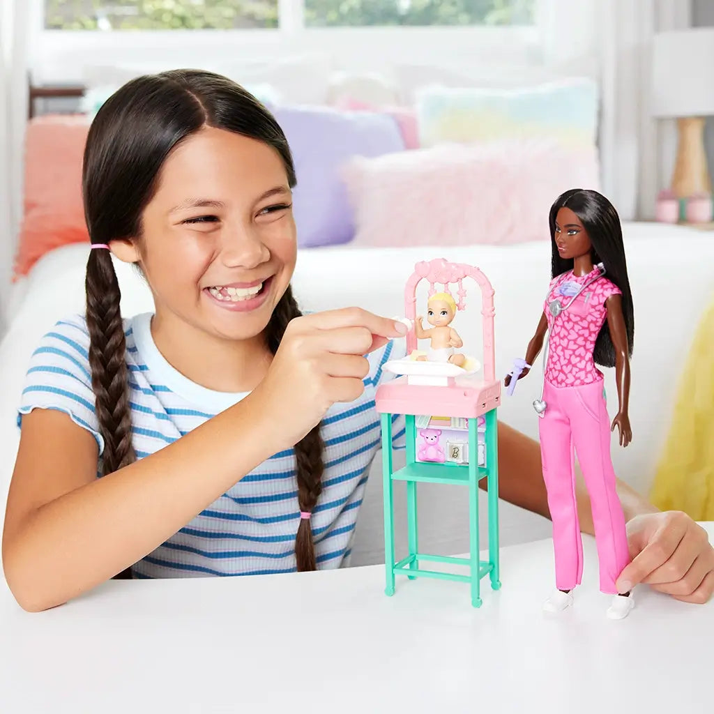 Smiling child plays with Barbie Baby Doctor set, using accessories to care for baby doll in pink and teal nursery station, encouraging imaginative roleplay and nurturing skills.