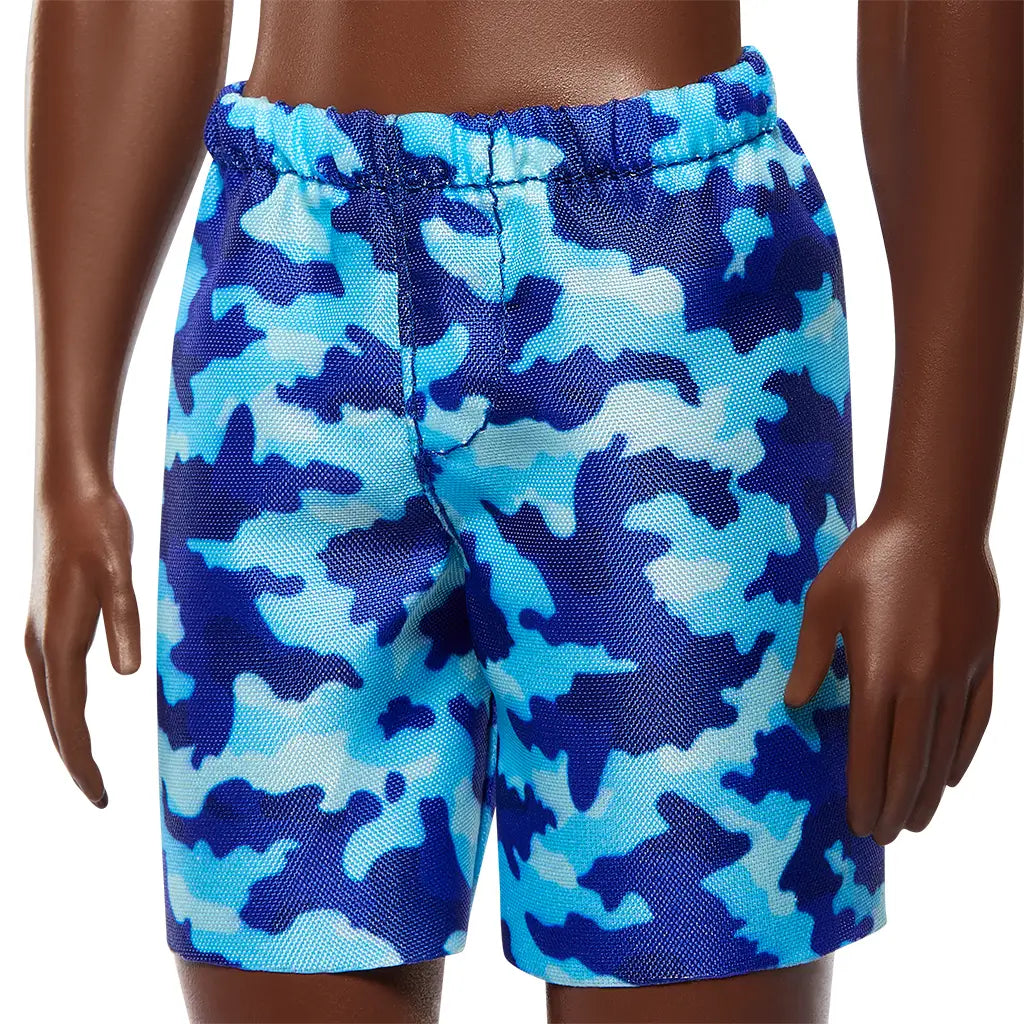 Close-up of Barbie Beach Ken doll’s blue and navy camouflage swim shorts with elastic waistband, featuring detailed stitching and vibrant beach-ready pattern.