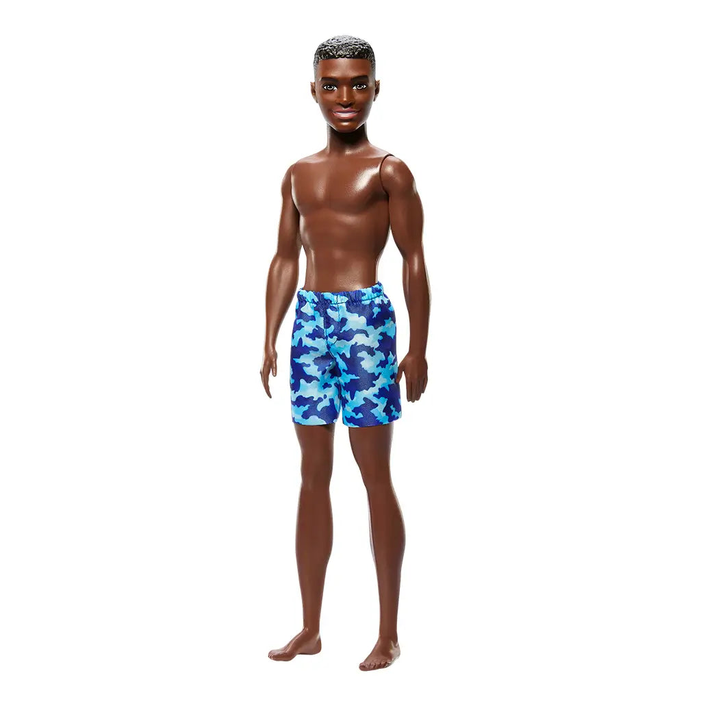 Full-body Barbie Beach Ken doll with deep brown skin, short textured brown hair, and blue camouflage swim shorts, posed barefoot against a white background.