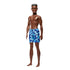 Full-body Barbie Beach Ken doll with deep brown skin, short textured brown hair, and blue camouflage swim shorts, posed barefoot against a white background.