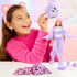 Smiling child wearing pink bear ear headband plays with Barbie Cutie Reveal doll dressed in a purple Care Bears costume, with surprise accessories and plush bear head on table.
