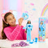 Smiling child unboxes Barbie Cutie Reveal Care Bears Grumpy Bear doll, holding bear costume head with accessories, doll, and rainbow-themed packaging displayed on tabletop.