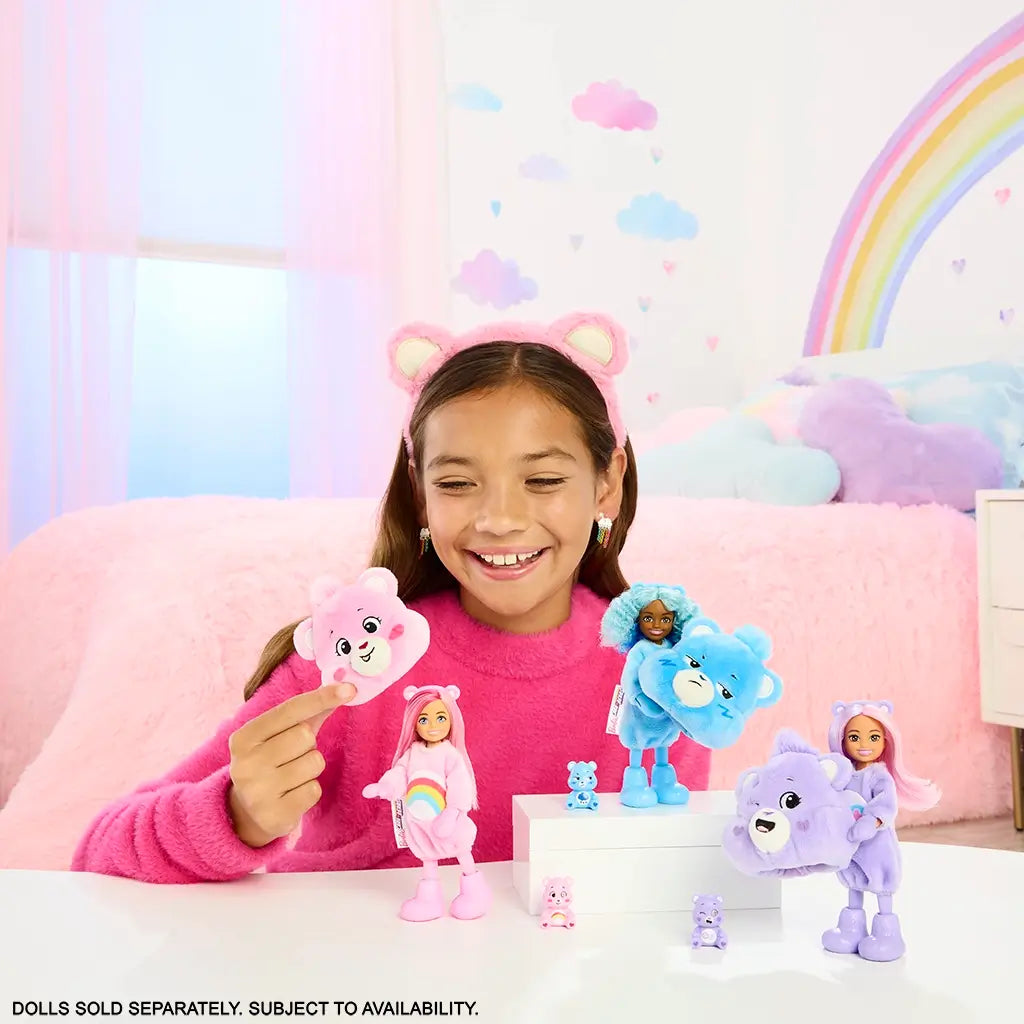 Smiling child in pink sweater and bear ear headband playing with Barbie Cutie Reveal Care Bears dolls, shown in pink, blue, and purple costumes in a pastel bedroom.