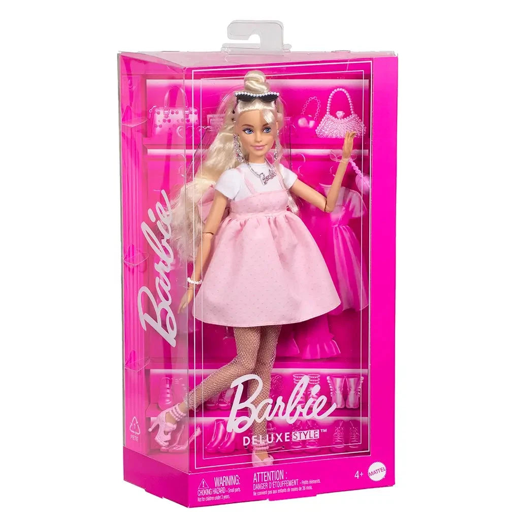 Barbie Deluxe Style fashion doll in pastel pink Barbiecore dress, displayed in pink packaging with accessories including purse, shoes, and jewelry.