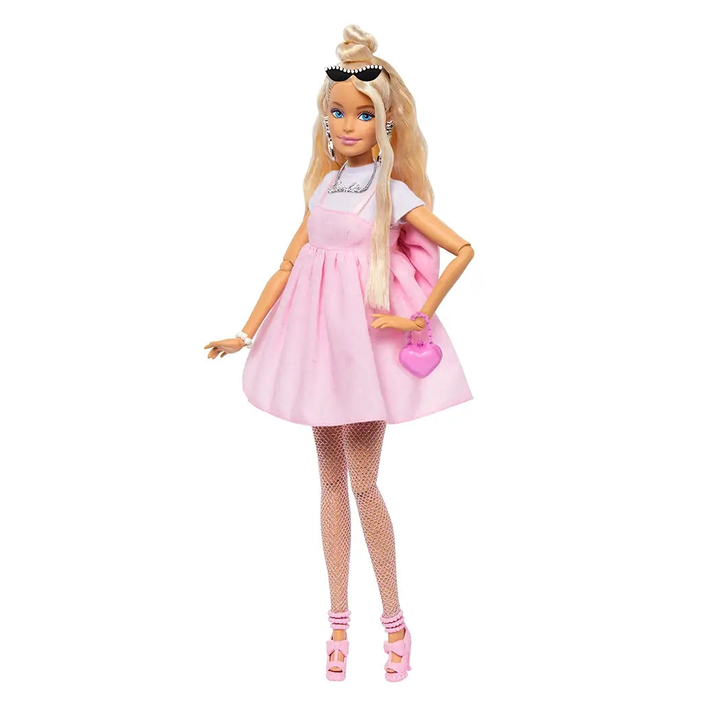 Barbie Deluxe Style doll wearing pastel pink dress, fishnet tights, pink heels, and holding a heart-shaped purse, styled with long blonde hair and accessories.