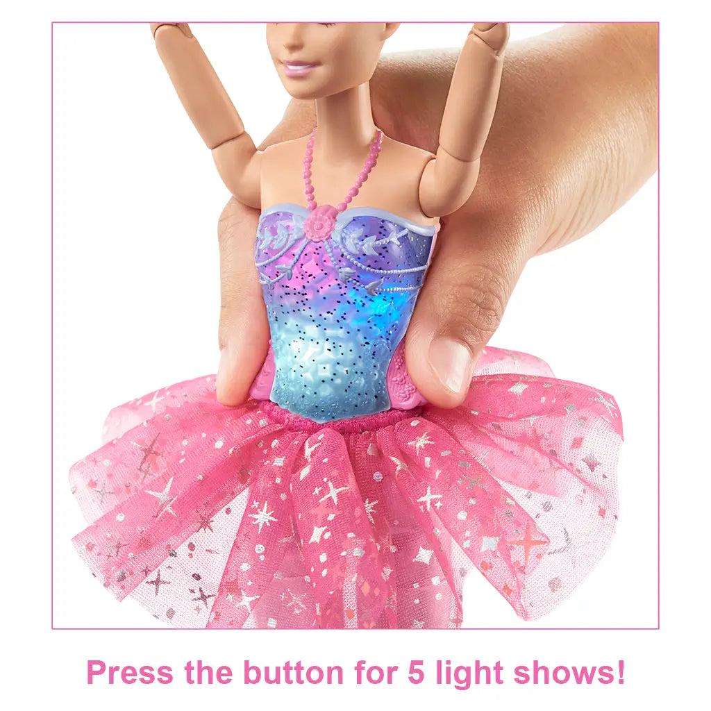 Barbie Dreamtopia Twinkle Lights Ballerina doll wearing a glittery purple bodice and pink star-patterned tutu, with a hand pressing her torso button to activate colorful light shows.