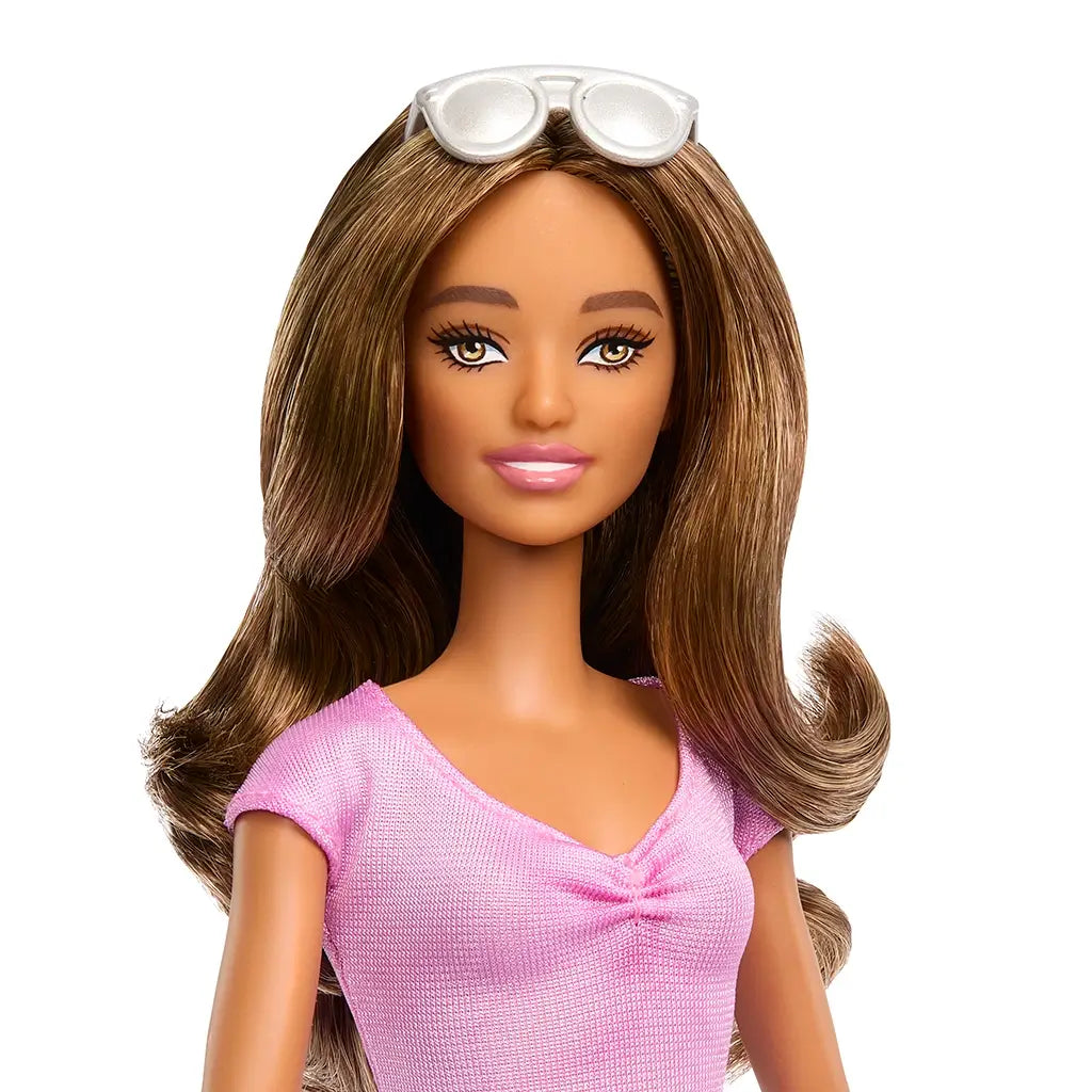 Close-up of Barbie Fashionistas doll with long brown hair, soft pink lips, and white sunglasses resting on her head while wearing a pink top with subtle ruching detail at the neckline.