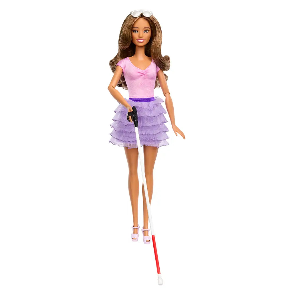 Barbie Fashionistas doll stands upright wearing a pink fitted top, purple layered ruffle skirt, pink sandals, and sunglasses, holding a white cane designed to represent vision impairment.