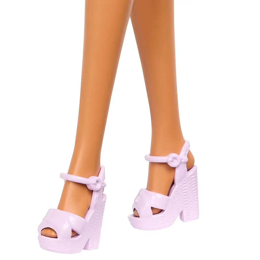 Light pink plastic platform sandals with open toes and ankle straps are shown on the Barbie doll’s feet, designed with a textured wedge heel to complete her fashionable look.