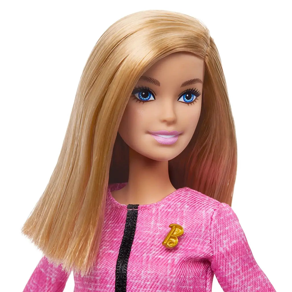 Close-up of Barbie Future Leader doll with straight blonde hair, blue eyes, and pink lipstick, wearing a textured pink jacket with gold B pin, promoting leadership and confidence.