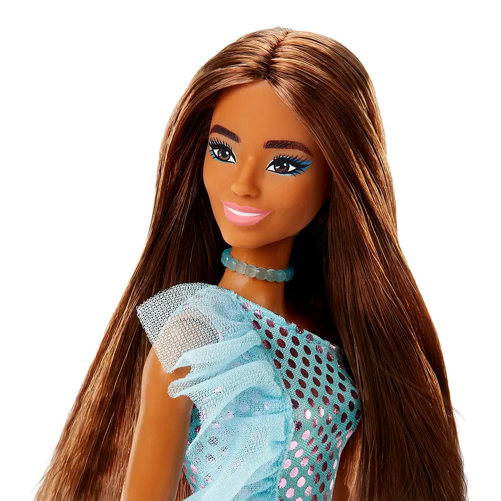 Barbie fashion doll with long straight brown hair wears a shimmering blue polka dot one-shoulder dress with mesh ruffle, matching choker, and pink lipstick against white backdrop.