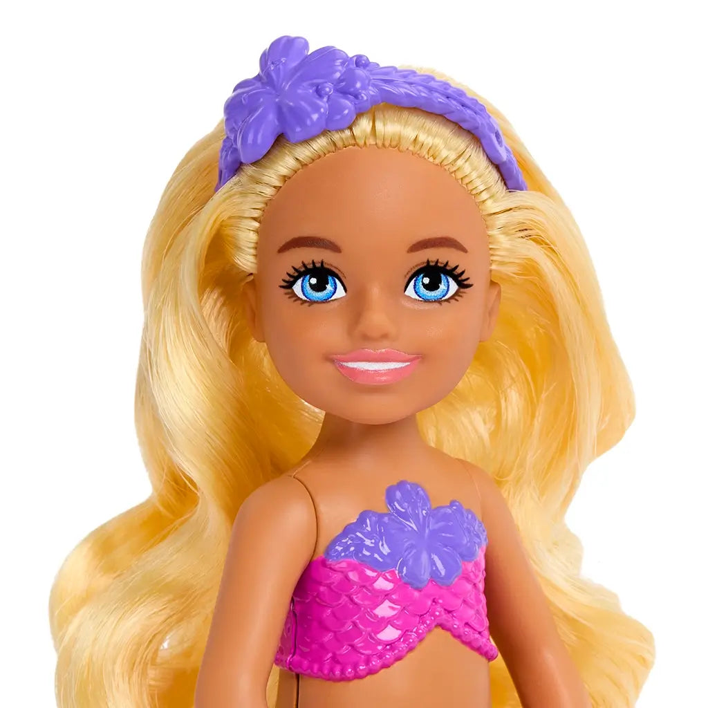 Close-up of Barbie Mermaid Chelsea doll’s face with blue eyes, pink lips, long blonde hair, and a purple hibiscus headband matching her mermaid top.