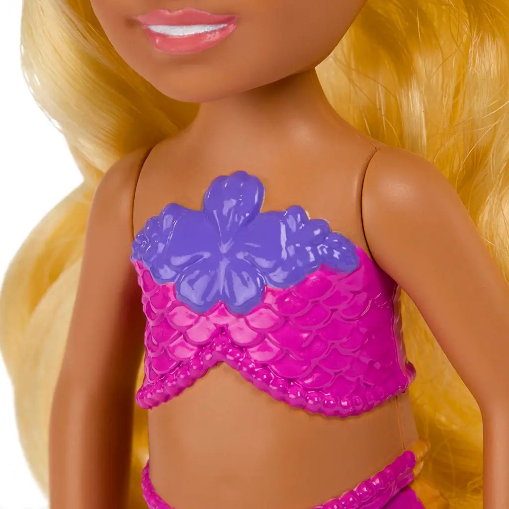 Close-up of Barbie Mermaid Chelsea doll’s torso, featuring a pink scale-patterned mermaid top with a purple hibiscus flower design and matching waistband.