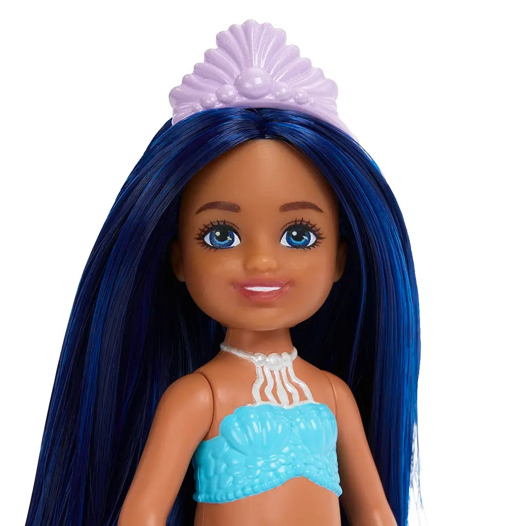 Barbie Chelsea mermaid doll with long blue hair, bright blue eyes, and a lavender seashell tiara wearing a textured aqua shell top and white coral-style necklace accessory.