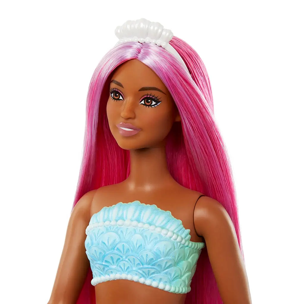Close-up of Barbie mermaid doll with smooth dark skin, magenta hair, pearl-like tiara, and a turquoise seashell-textured bandeau top, highlighting facial features and details.