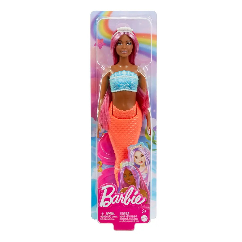 Barbie mermaid doll in retail packaging with rainbow backdrop, featuring magenta hair, turquoise shell top, and red mermaid tail, with branding and product details at bottom.