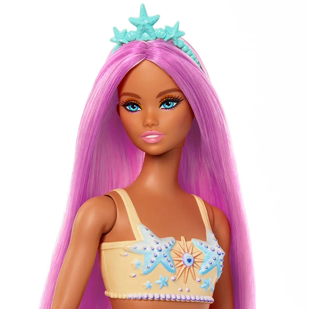 Close-up of Barbie mermaid doll with long pink hair, blue starfish tiara, bright blue eyes, and detailed peach top decorated with sea-themed accents.