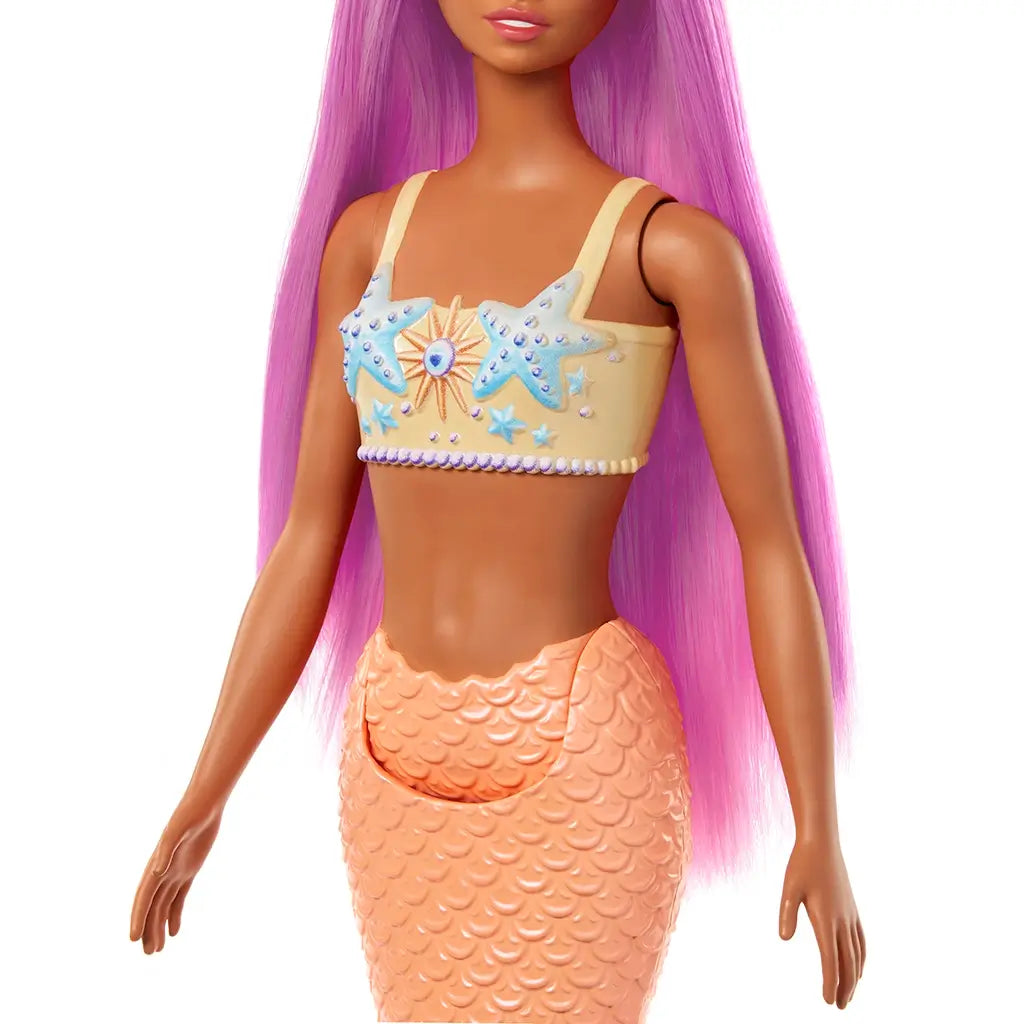 Close-up of Barbie mermaid doll’s torso showing peach starfish top with blue accents, orange scaled mermaid tail, and long flowing pink hair.