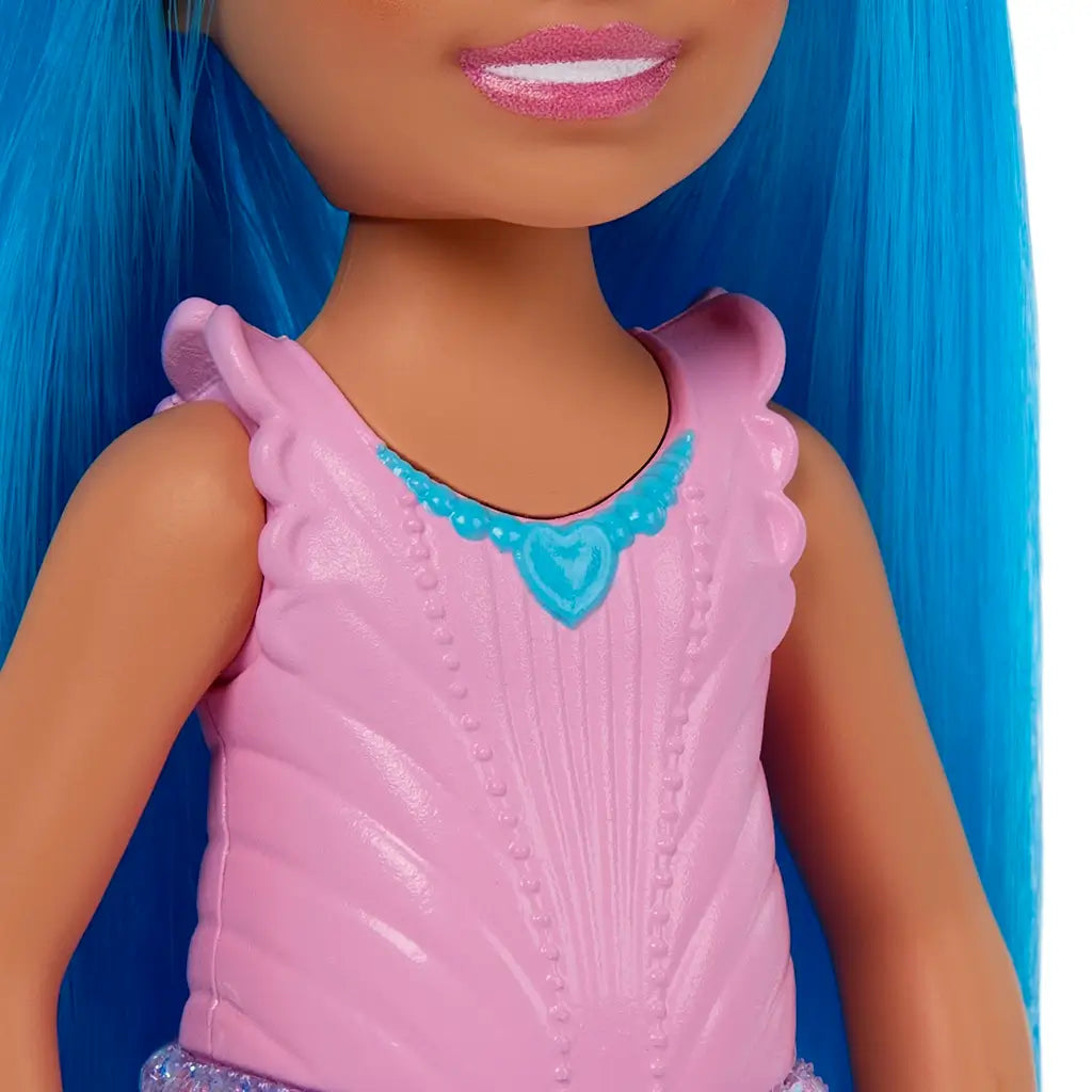 Close-up of Barbie Chelsea doll’s pink textured bodice with ruffled straps, featuring a molded blue heart pendant detail, shown with her bright blue hair framing the outfit.