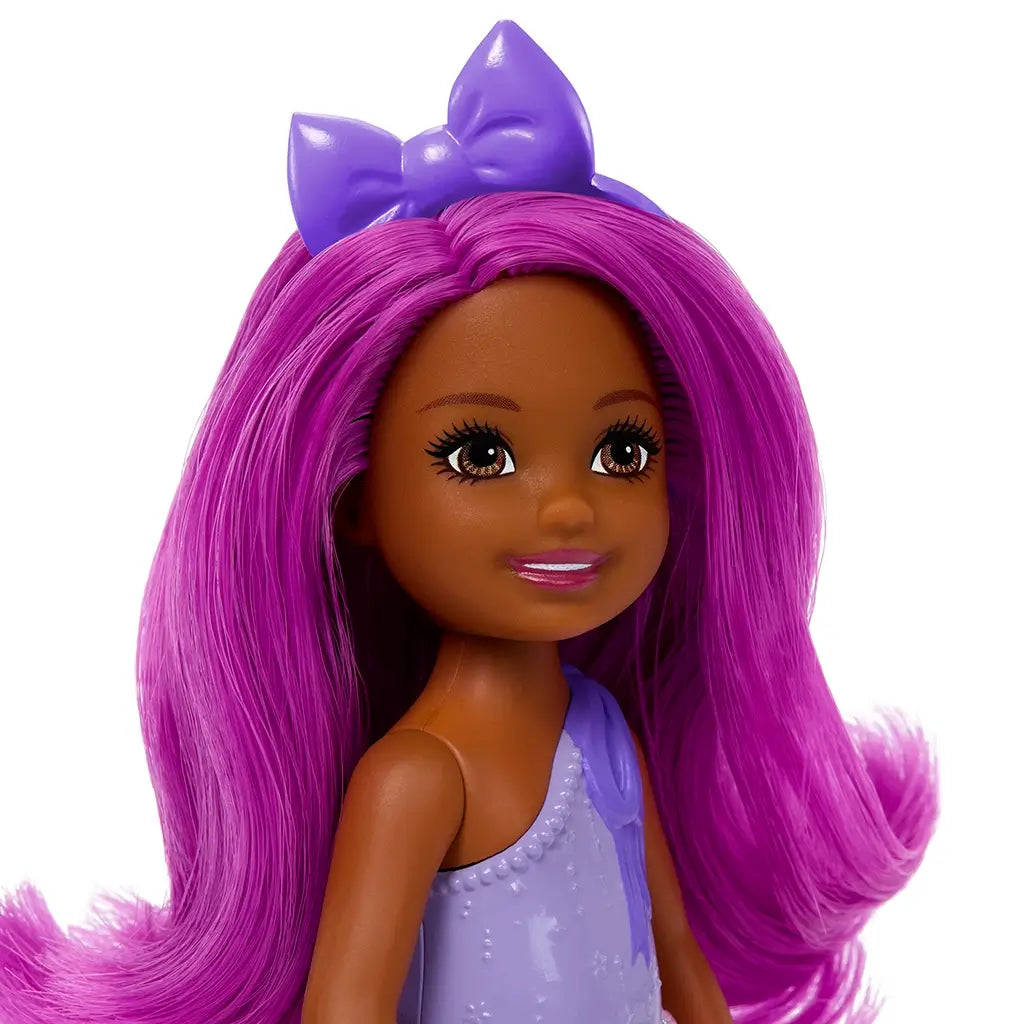 Closeup of Barbie Chelsea doll’s face with deep brown skin, large brown eyes, bright pink lips, long vibrant magenta hair, and a shiny purple bow headband.