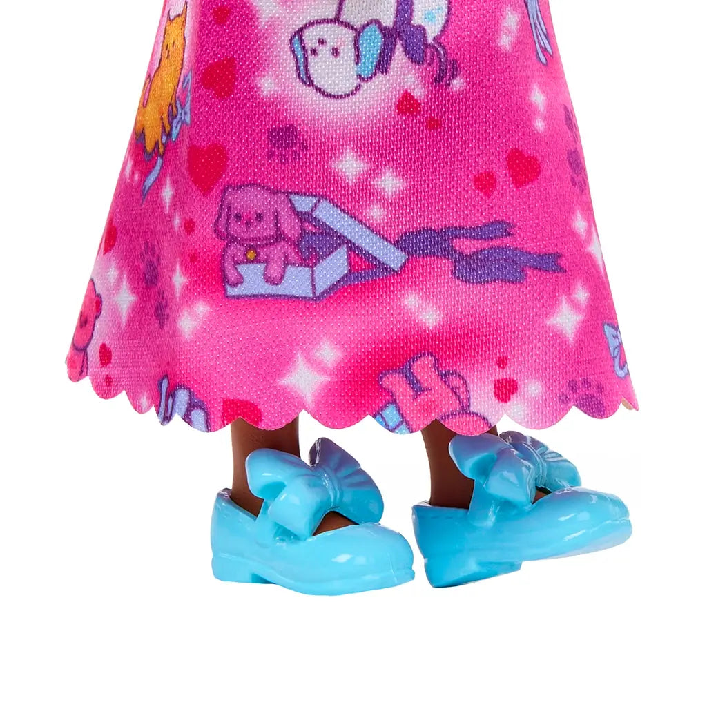 Closeup of Barbie Chelsea doll’s lower skirt hem with scalloped edge, showing colorful dog and gift box designs, paired with glossy blue shoes featuring large bows.