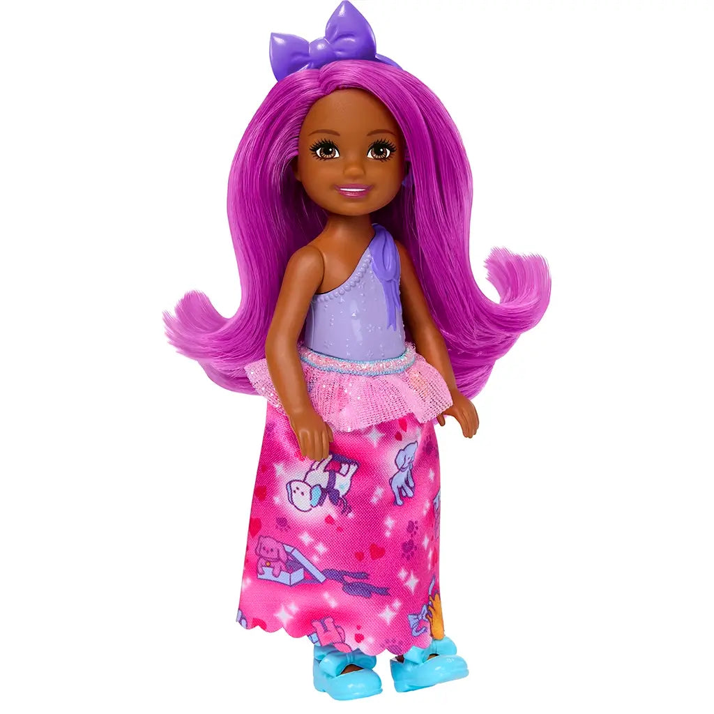 Full view of Barbie Chelsea doll with magenta hair, purple bow, lilac top, pink tutu, long pink skirt featuring dog print, and bright blue bow shoes.