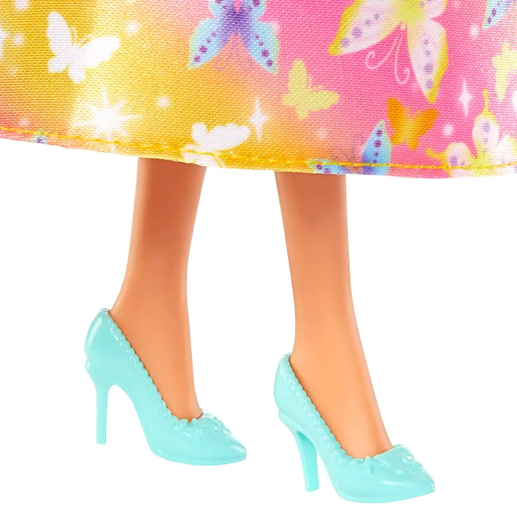 Close-up of Barbie doll’s feet wearing glossy mint high-heeled shoes with scalloped edges and butterfly details, shown under a colorful butterfly-print skirt.