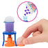 Close-up of Barbie science experiment accessory with toy beaker on orange and blue stand, showing purple liquid bubbling after purple heart tablets are added from holographic packet above.