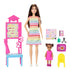 Barbie Teacher fashion doll set with brunette doll in rainbow zigzag dress, student doll in pink dress, chalkboard, yellow chair, and classroom play accessories.